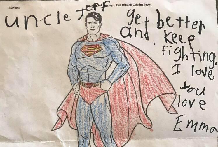 A child's coloring book image of Superman with a handwritten note that says, "Uncle Jeff, get better and keep fighting. I love you. Emma."
